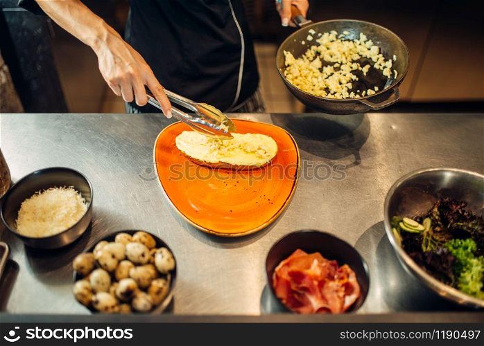 Female chef with pan cooking meat with pasta on wooden table. Garnish for beefsteak, food preparation on kitchen. Female chef with pan cooking meat with pasta