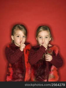 Female children Caucasian twins with fingers up to lips.