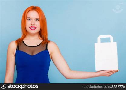 Female client customer red hair woman presenting white paper shopping bag with copy space for text,. Retail sale and advertisement. Studio shot on blue.