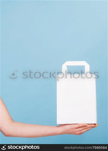 Female client customer woman presenting white paper shopping bag with copy space for text,. Retail sale and advertisement. Studio shot on blue.