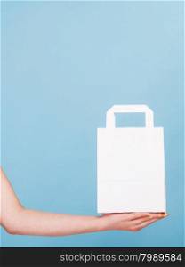 Female client customer woman presenting white paper shopping bag with copy space for text,. Retail sale and advertisement. Studio shot on blue.