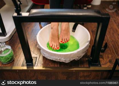 Female client feet in a pedicure bath, top view, cosmetic procedure in nail salon. Professional fingernail and foot skin care. Female client feet in a pedicure bath, top view