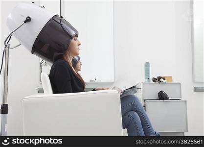 Female client sits under drying hood in hair salon