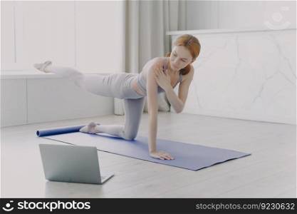 Female coach explaining at video class. Young athlete practicing yoga by video lessons in her apartment. White woman doing posture exercise. Concept of personal training and remote work.. Woman coach has video class. Young athlete practicing yoga. Personal training by video lessons.