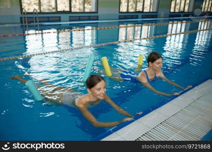 Female coach instructing young woman exercising with pool noodle aerobics class. Fitness sport activity for health and wellbeing in swimming pool. Female coach instructing young woman exercising with pool noodle aerobics class