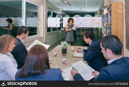 Female coach talking while looking project management to business team sitting at table in headquarters. Female coach looking project management in business team training