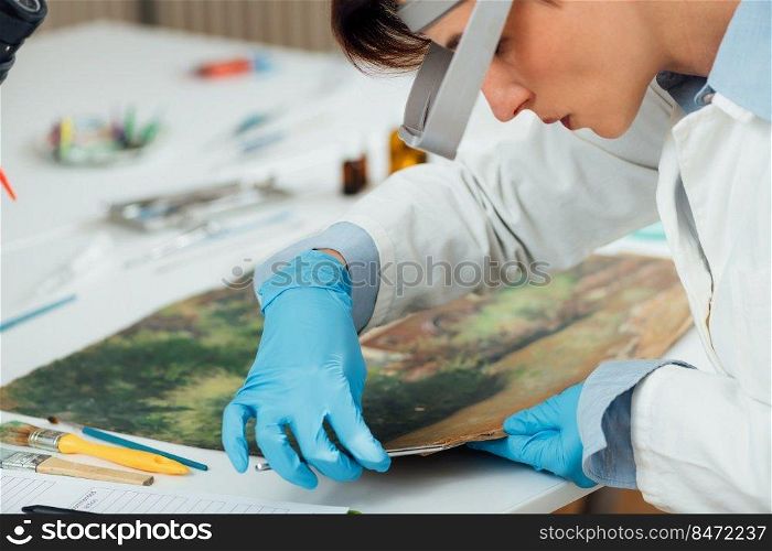 Female conservator with magnifying goggles cleaning dirt from antique oil painting . Repairing Antique Oil Painting