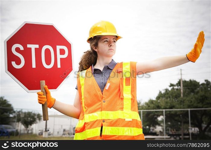 Female construction apprentice holding a stop sign and directing traffic.