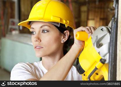 Female construction worker cutting wood with a power saw while looking away