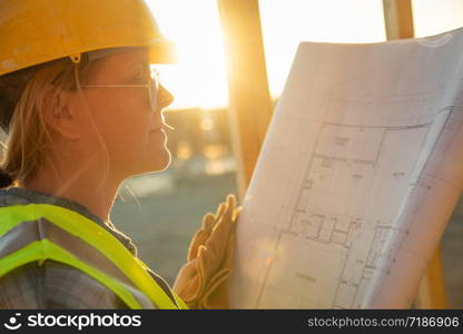 Female Construction Worker with House Plans at Construction Site.
