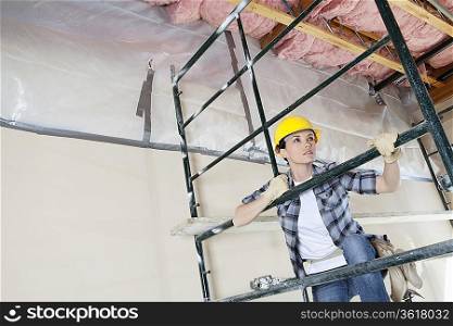 Female contractor climbing scaffold while looking away at construction site