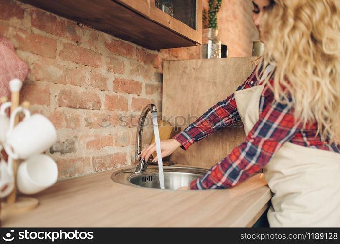 Female cook in apron washes fresh vegetables, kitchen interior on background. Housewife making healthy vegetarian food, salad preparation. Female cook in apron washes fresh vegetables
