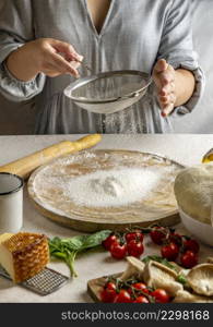 female cook sieving flour wooden board rolling pizza dough