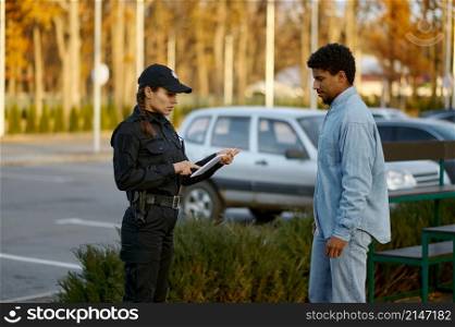 Female cop in black uniform checking male passerby ID document on the street. Female cop checking male passerby ID document