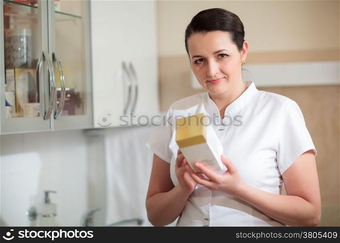 Female cosmetician holding a box with cosmetic to check information on it