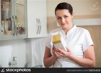 Female cosmetician holding a box with cosmetic to check information on it