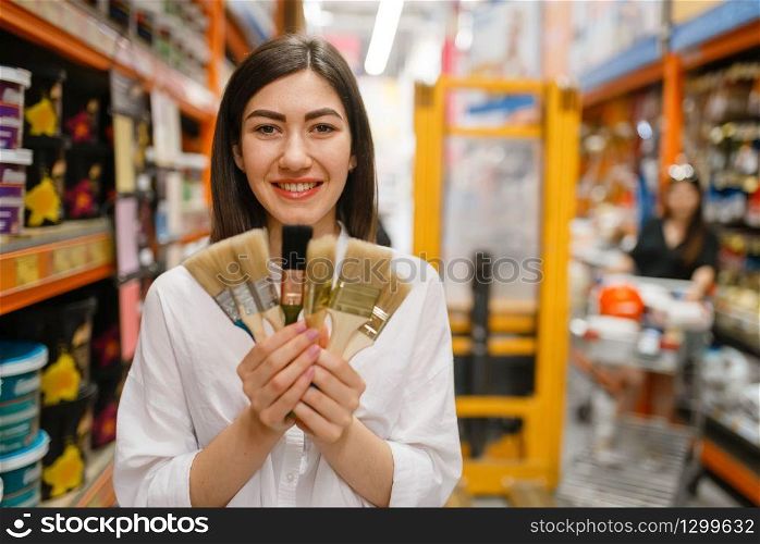 Female customer choosing brush in hardware store. Buyer look at the goods in diy shop, shopping in building supermarket