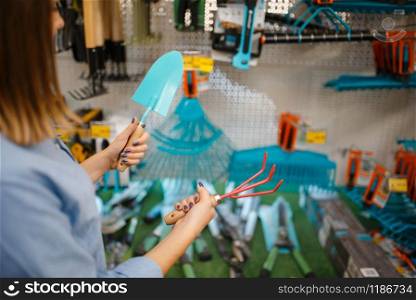 Female customer choosing garden shovel in shop for gardeners. Woman buying equipment in store for floriculture, florist instrument purchasing. Customer choosing garden shovel, gardeners shop