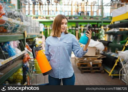 Female customer choosing garden spray in shop for gardeners. Woman buying equipment in store for floriculture, florist instrument purchasing