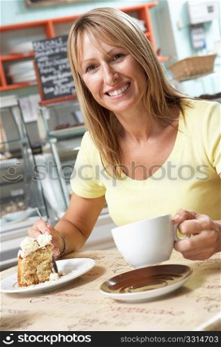 Female Customer Enjoying Slice Of Cake And Coffee In Cafe