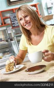 Female Customer Enjoying Slice Of Cake And Coffee In Cafe
