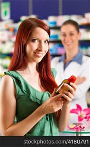 Female customer in a pharmacy - in the background the pharmacist