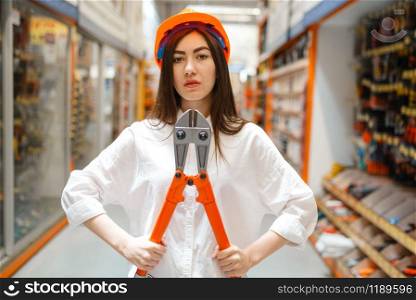 Female customer in helmet choosing metal wire cutters in hardware store. Buyer look at the goods in diy shop, shopping in building supermarket