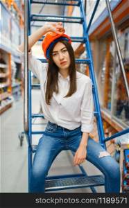 Female customer in helmet sitting on the stairs in hardware store. Buyer look at the goods in diy shop, shopping in building supermarket. Female customer sitting on stairs, hardware store