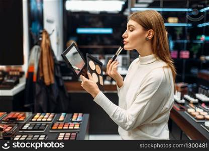 Female customer looks at the mirror in the makeup shop. Nail varnish choosing in beauty store, make-up salon. Female customer looks at the mirror in makeup shop