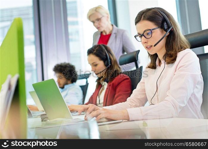 Female customer service representative using laptop while colleagues in background at office