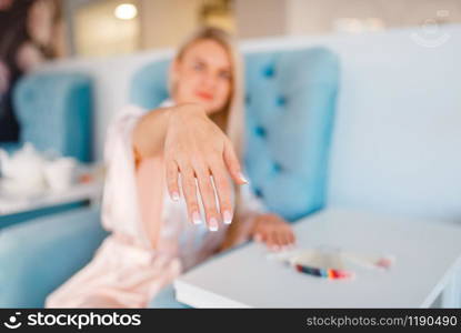 Female customer shows perfectly made nails in beauty shop. Professional manicure and pedicure service, hands and legs treatment, client in beautician salon, woman at the manicurist. Customer shows perfectly made nails in beauty shop