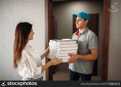 Female customer takes order from pizza delivery boy, fast delivering service. Courier from pizzeria carrying carton boxes and woman at the door. Customer takes order from pizza delivery boy