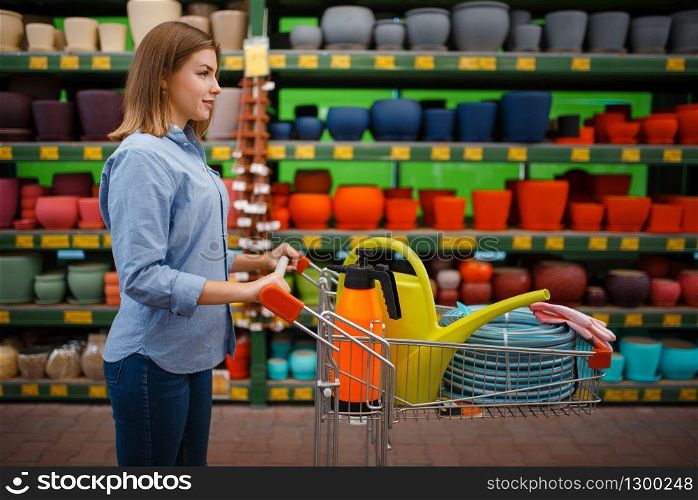 Female customer with cart buying tools for gardening. Woman choosing equipment in store for floriculture, florist instrument purchasing. Female customer buying tools for gardening