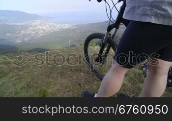Female cyclist with mountain bike stands on top of the mountain Ai-Petri, Yalta, Crimea vertical dolly shot