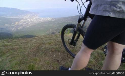 Female cyclist with mountain bike stands on top of the mountain Ai-Petri, Yalta, Crimea vertical dolly shot