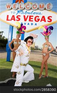 Female dancers and Elvis impersonator posing in front of Las Vegas welcome sign, Nevada, USA