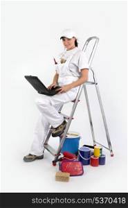 Female decorator perched on ladder to use laptop