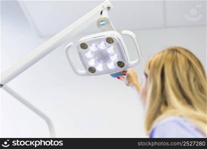 female dentist adjusting medical lamp clinic