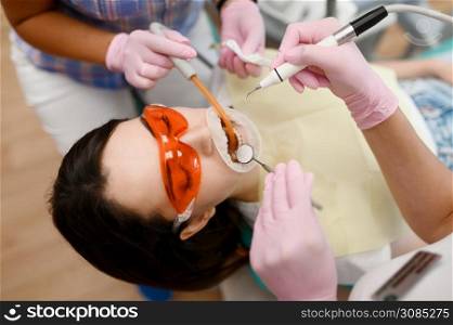 Female dentist and assistant are treats patient in clinic, stomatology. Doctor in uniform, medical worker, medicine and health, professional teeth care, dentistry. Dentist and assistant are treats patient in clinic
