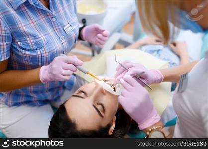 Female dentist and assistant works with patient in clinic, stomatology. Doctor in uniform, medical worker, medicine and health, professional teeth care, dentistry. Female dentist and assistant works with patient