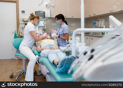 Female dentist and assistant works with patient in clinic, stomatology. Doctor in uniform, medical worker, medicine and health, professional teeth care, dentistry. Female dentist and assistant works with patient