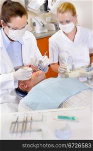 Female dentist and nurse doing operation on male patient