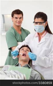 Female dentist examining man&rsquo;s teeth in dental office with assistant behind