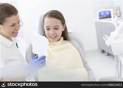 Female dentist showing mirror to smiling patient at clinic