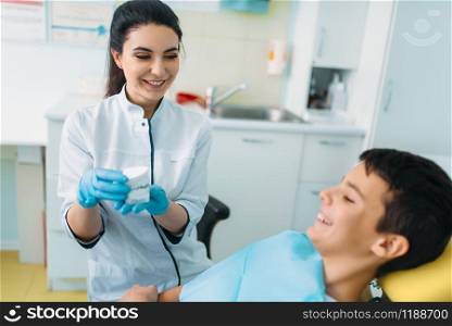 Female dentist shows dentures to little boy in a dental chair, professional pediatric dentistry, children stomatology. Female dentist shows dentures to little boy
