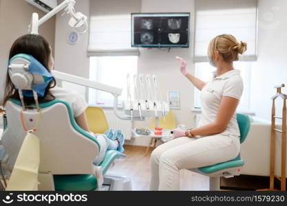 Female dentist shows to patient x-ray of teeth, stomatology clinic. Doctor in uniform, medical worker, stomatologist, medicine and health, professional dental mouth care and hygiene, dentistry. Female dentist shows to patient x-ray of teeth