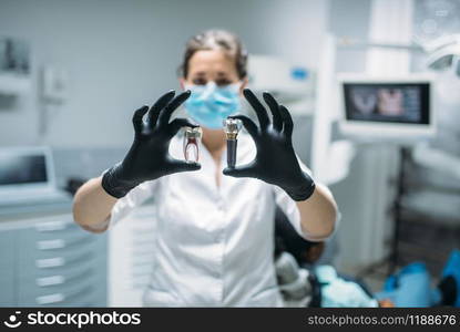 Female dentist shows tooth pin and model, dental clinic, professional prosthetic dentistry, stomatology cabinet, odontology