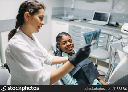 Female dentist shows x-ray picture to patient, dental clinic. Woman in dentistry cabinet, stomatology, teeth care