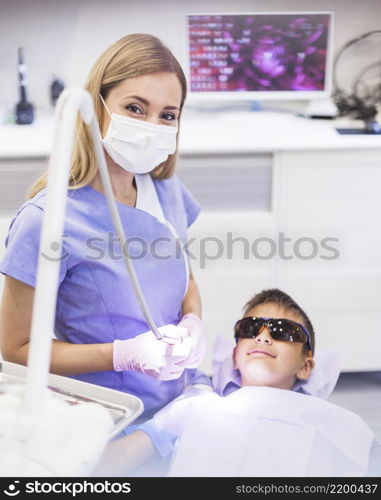 female dentist standing near boy wearing safety protective glasses