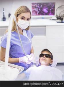female dentist standing near boy wearing safety protective glasses